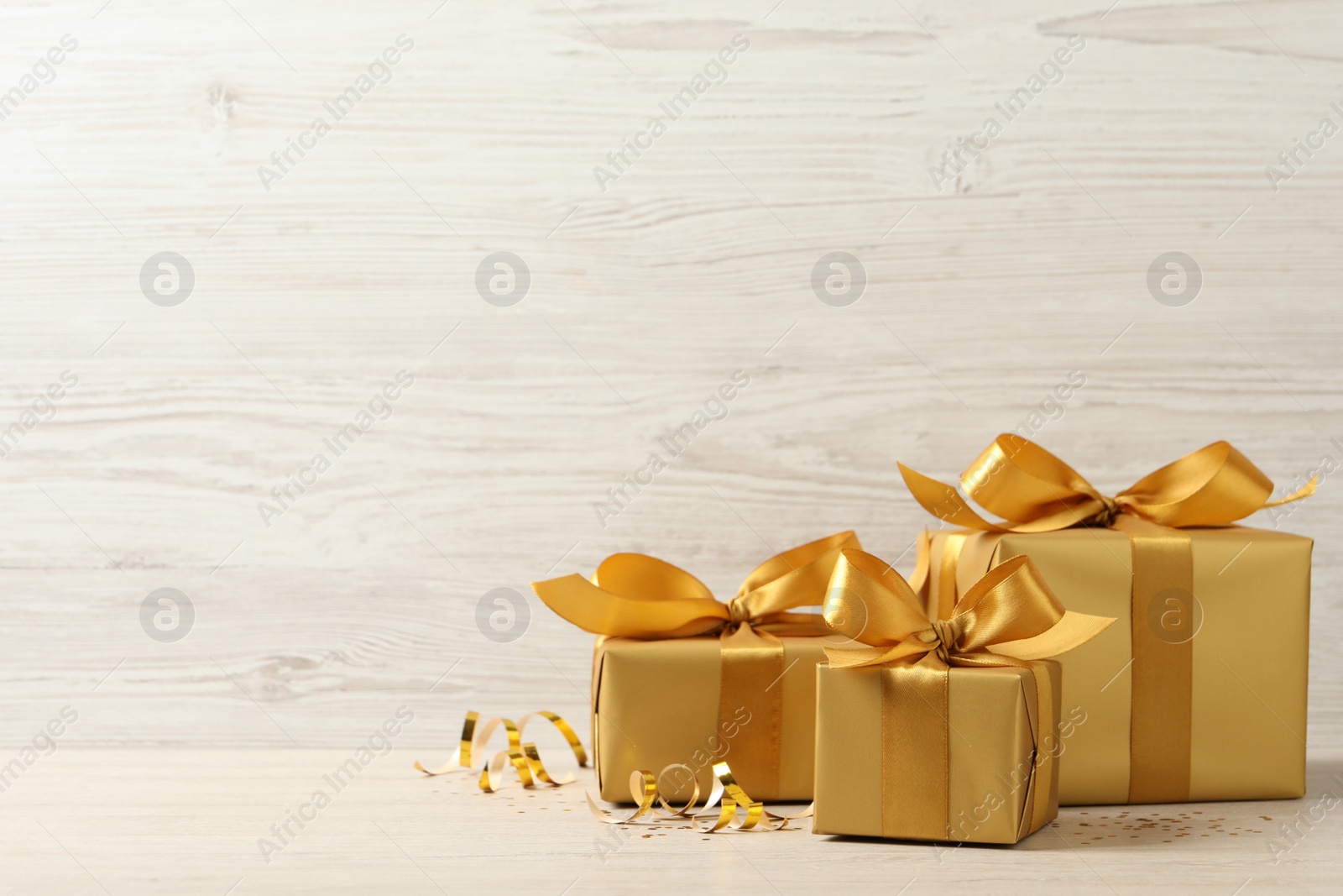 Photo of Beautifully wrapped gift boxes and confetti on white wooden table, space for text