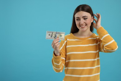 Sad woman with dollar banknote on light blue background, space for text