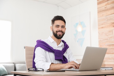 Photo of Handsome young man working with laptop at table in home office