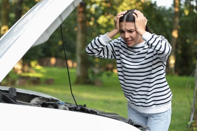 Stressed young woman near broken car outdoors