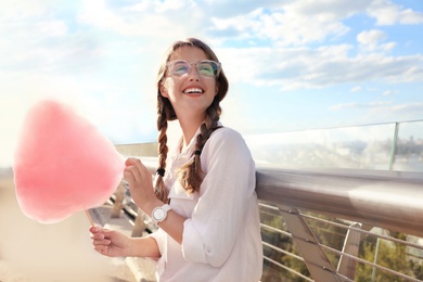 Photo of Young woman with cotton candy outdoors on sunny day. Space for text