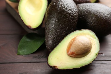 Whole and cut avocados on wooden table, closeup