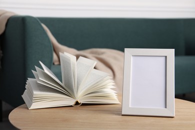 Photo of Empty square frame and book on wooden table indoors