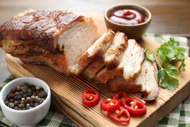 Photo of Pieces of baked pork belly served with sauce, chili pepper and parsley on wooden table, closeup