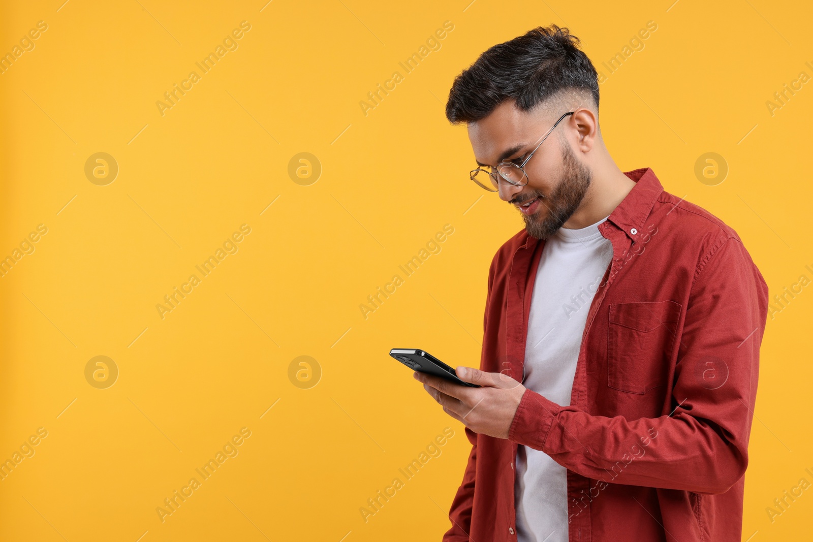 Photo of Handsome young man using smartphone on yellow background, space for text