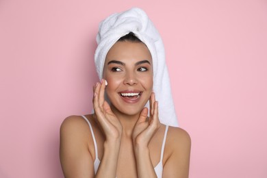 Photo of Beautiful young woman with towel applying cream on face against pink background