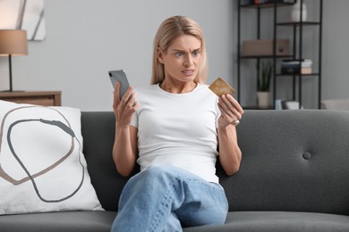 Stressed woman with credit card and smartphone on sofa at home. Be careful - fraud