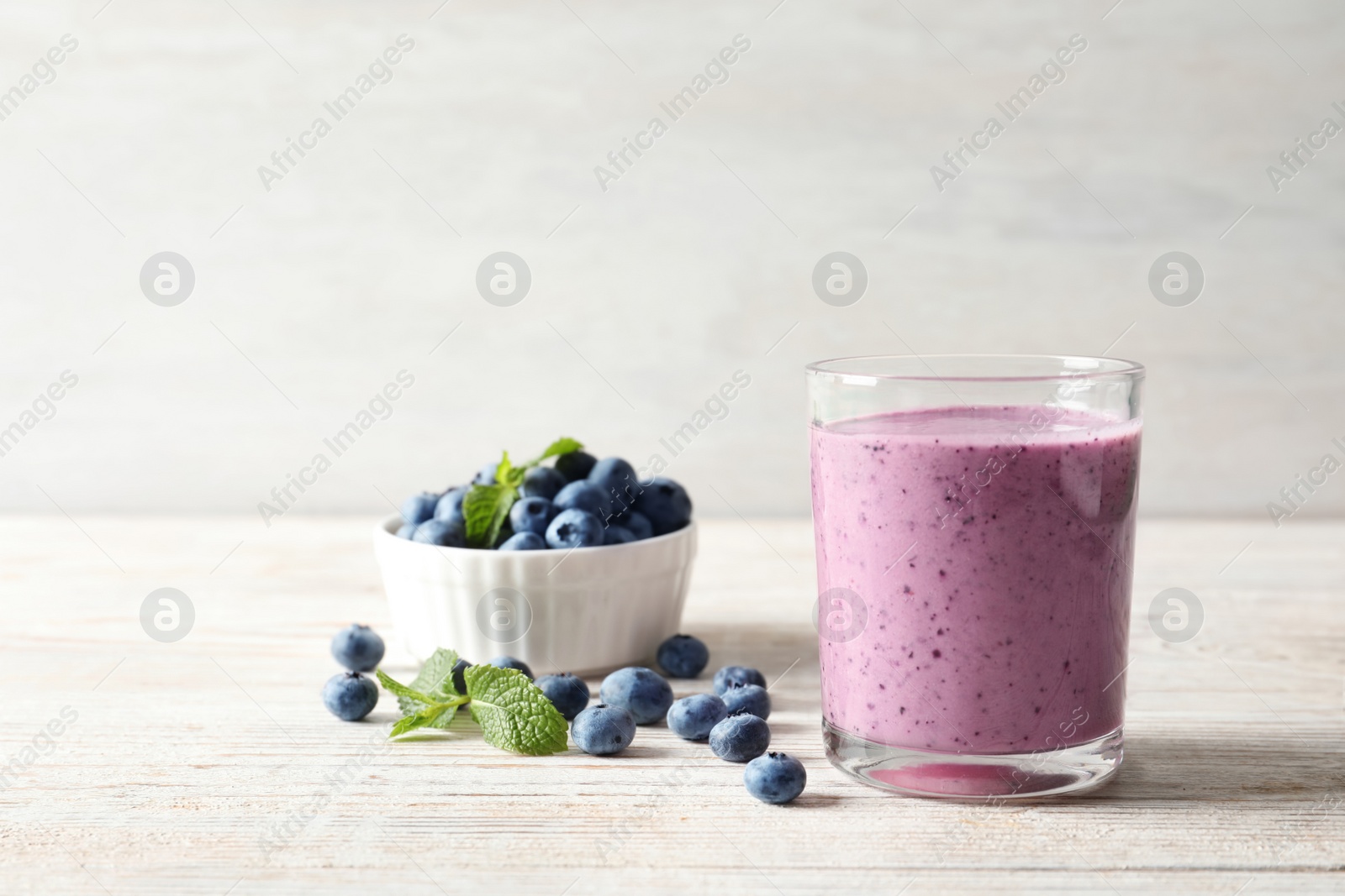 Photo of Tasty blueberry smoothie in glass, bowl with berries on table against light background with space for text