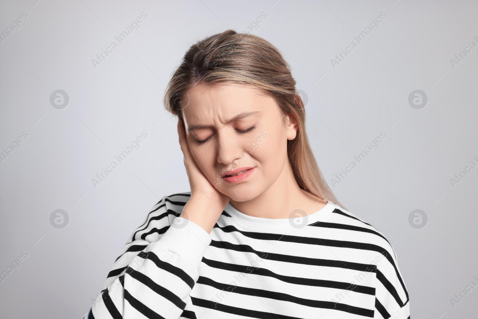 Photo of Young woman suffering from ear pain on light grey background