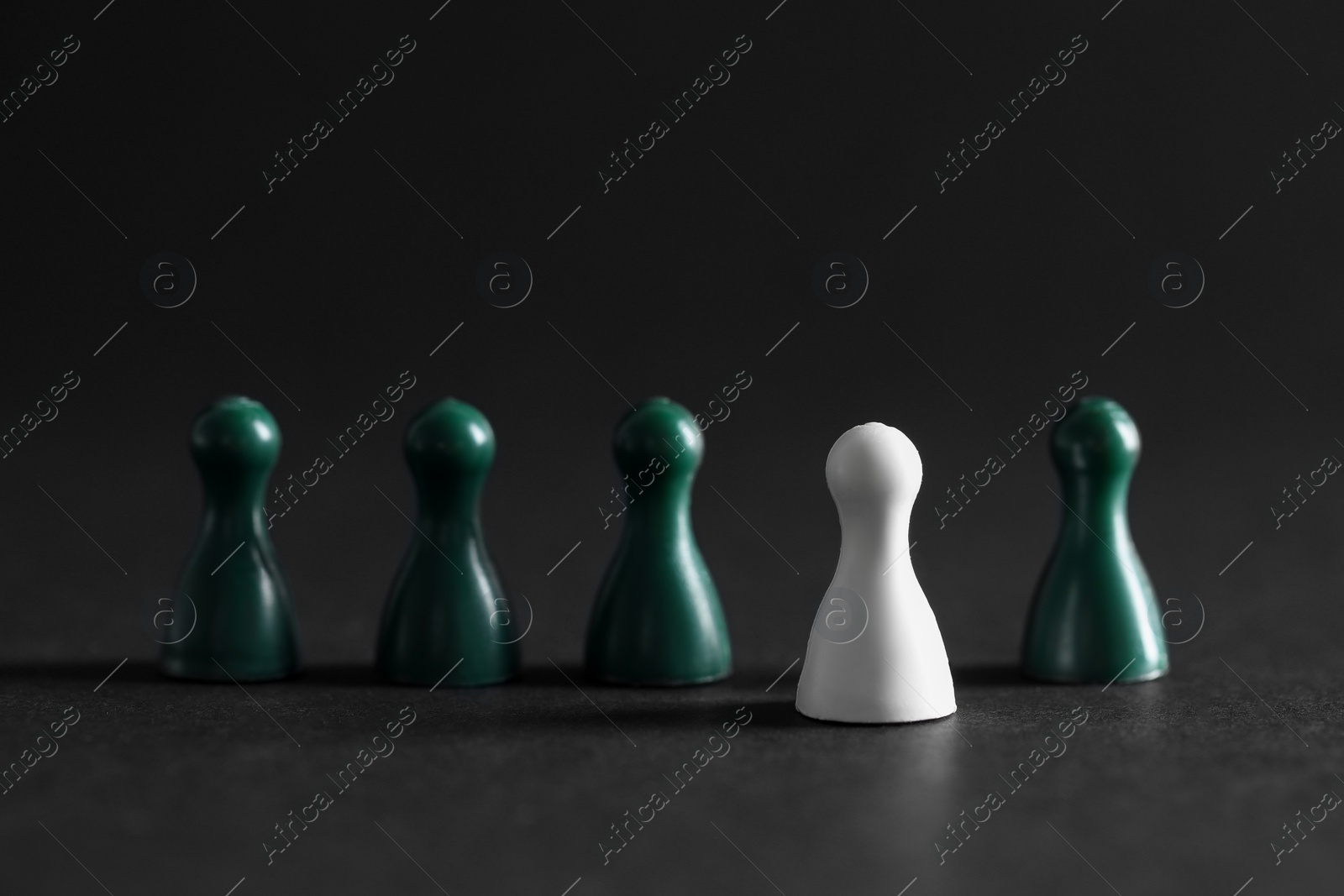 Photo of Choice concept. White pawn and green ones on dark table, closeup