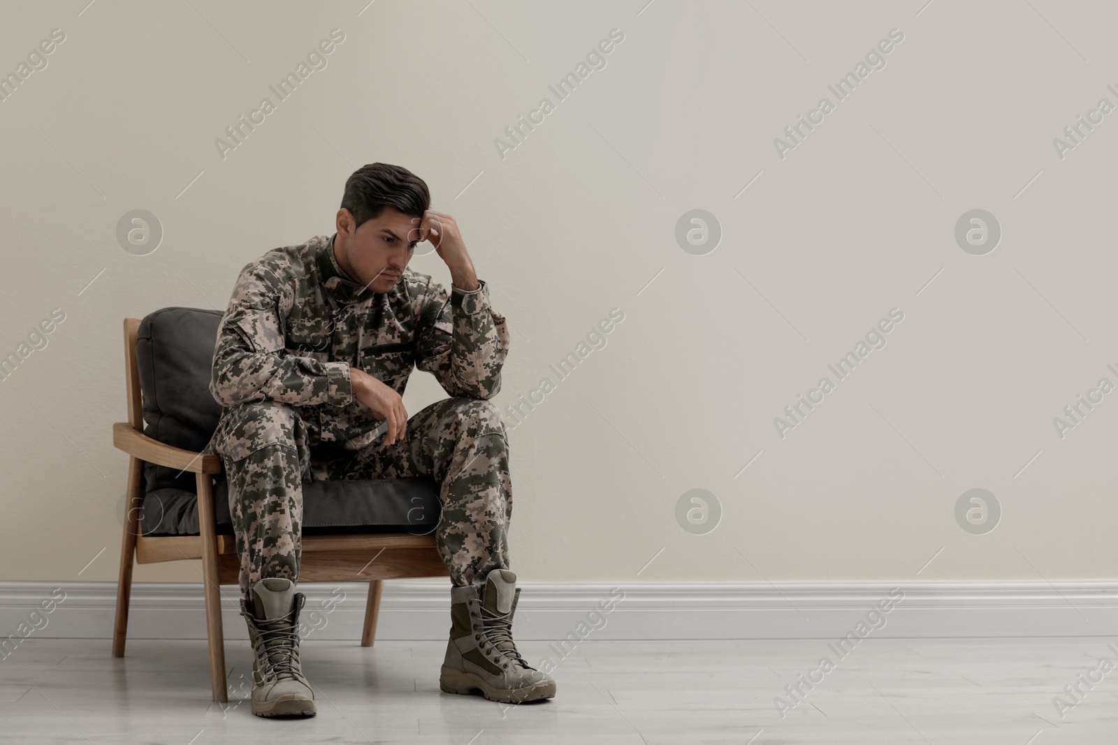 Photo of Stressed military officer sitting in armchair near white wall indoors. Space for text