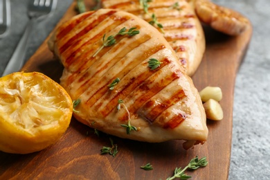 Tasty grilled chicken fillets with lemon and thyme on wooden board, closeup