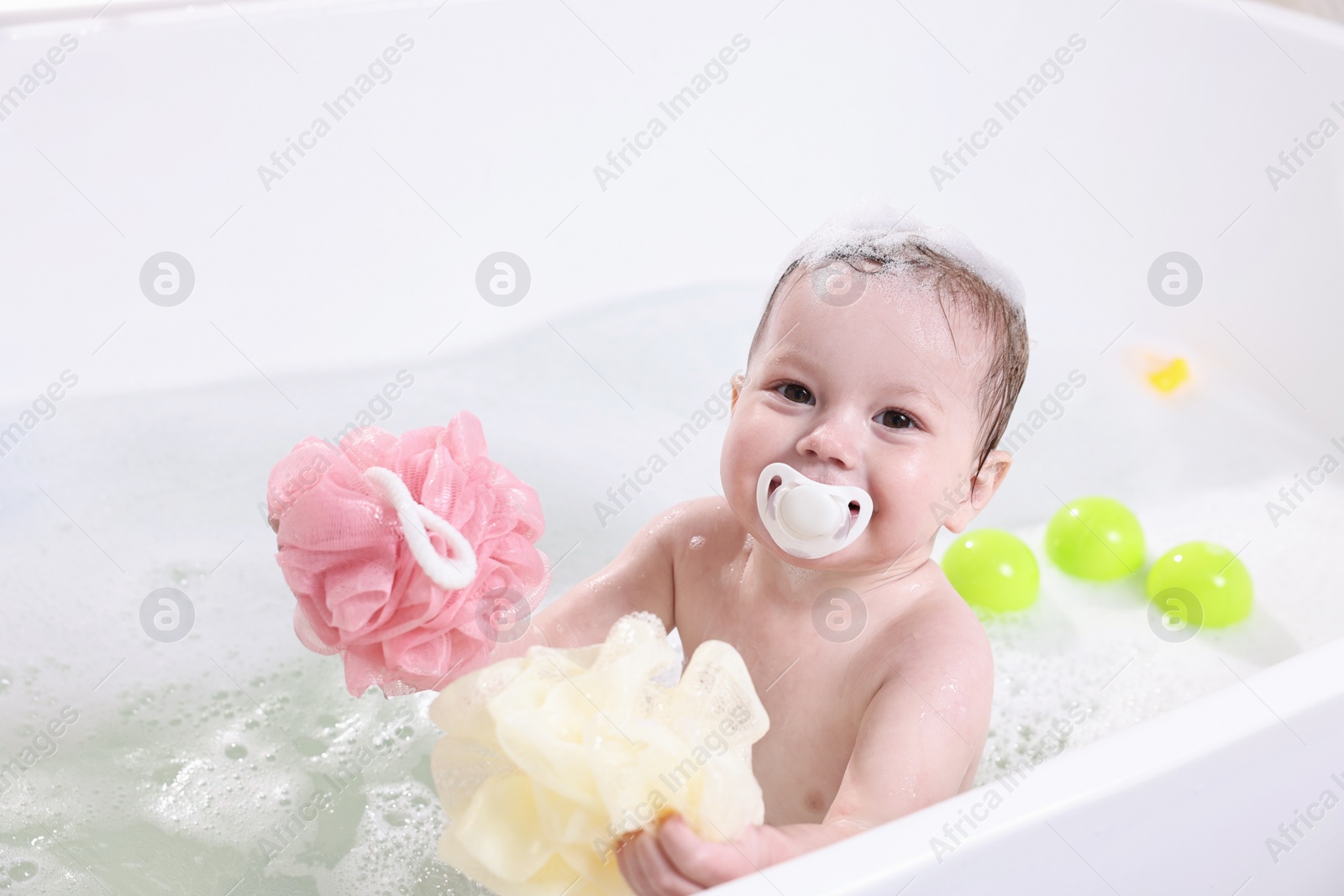 Photo of Cute little child bathing with sponges in tub at home