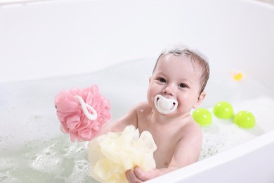 Cute little child bathing with sponges in tub at home