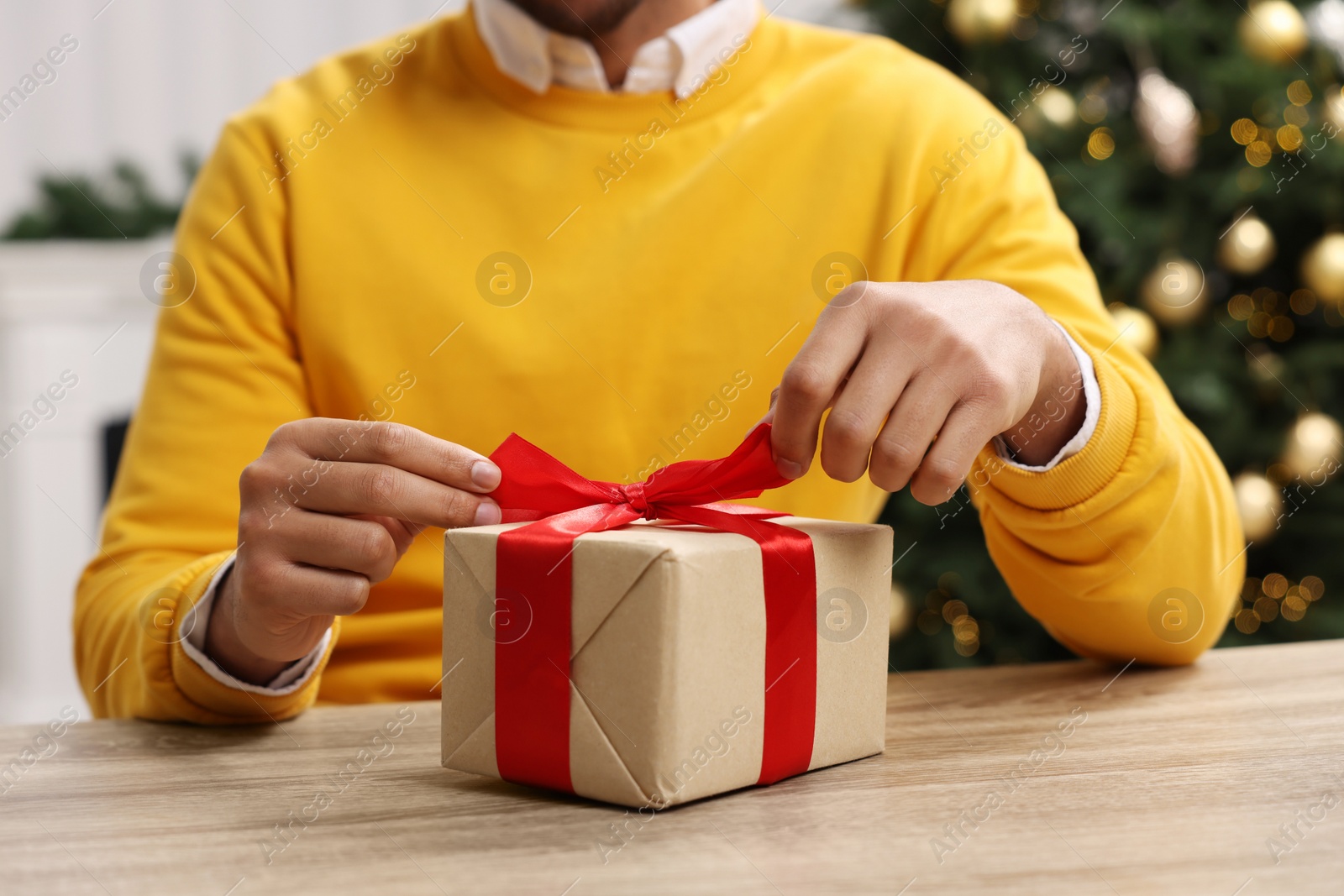 Photo of Man opening Christmas gift box at wooden table indoors, closeup