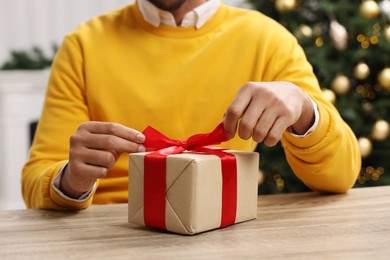 Man opening Christmas gift box at wooden table indoors, closeup