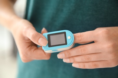 Young woman checking pulse with blood pressure monitor on finger, closeup