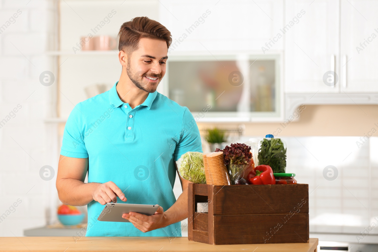 Photo of Young man with tablet PC and products in kitchen. Food delivery service