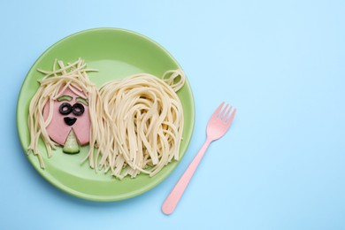Photo of Creative serving for kids. Plate with cute dog made of tasty pasta, sausage and cucumber on light blue table, flat lay. Space for text
