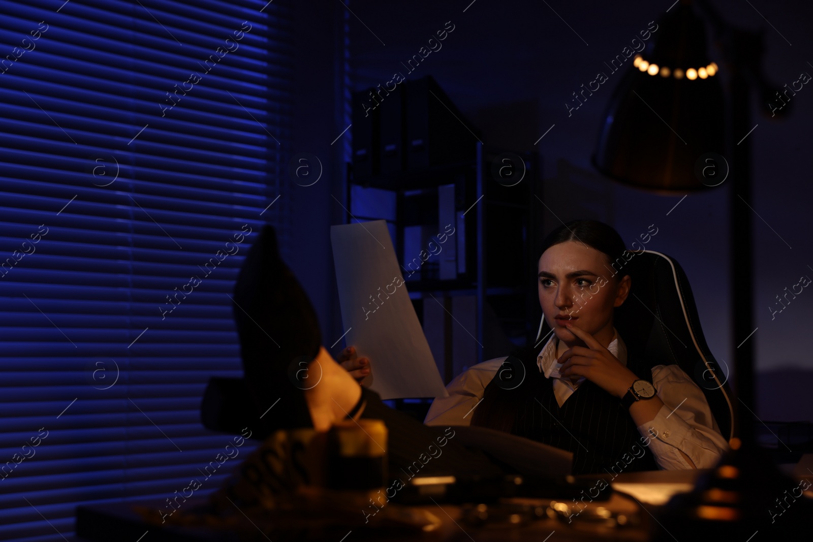 Photo of Professional detective working with documents at table in office at night