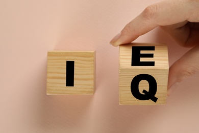 Photo of Woman turning cube with letters E and I near Q on beige background, top view