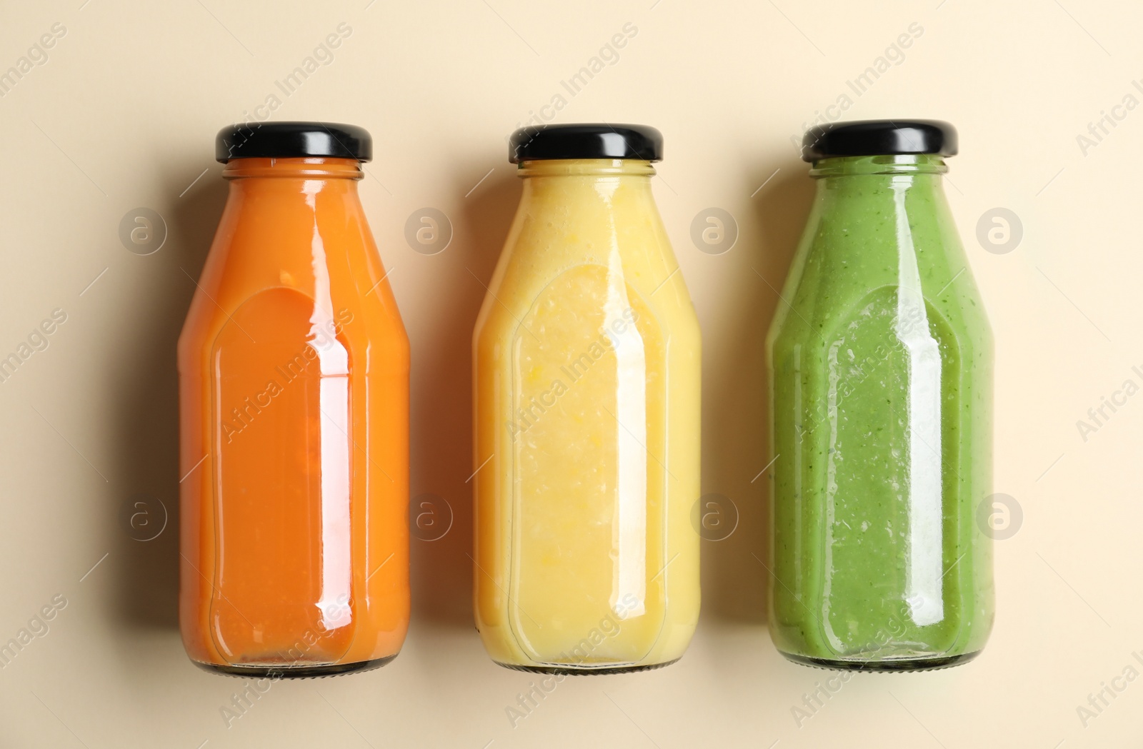 Photo of Bottles with delicious colorful juices on beige background, flat lay