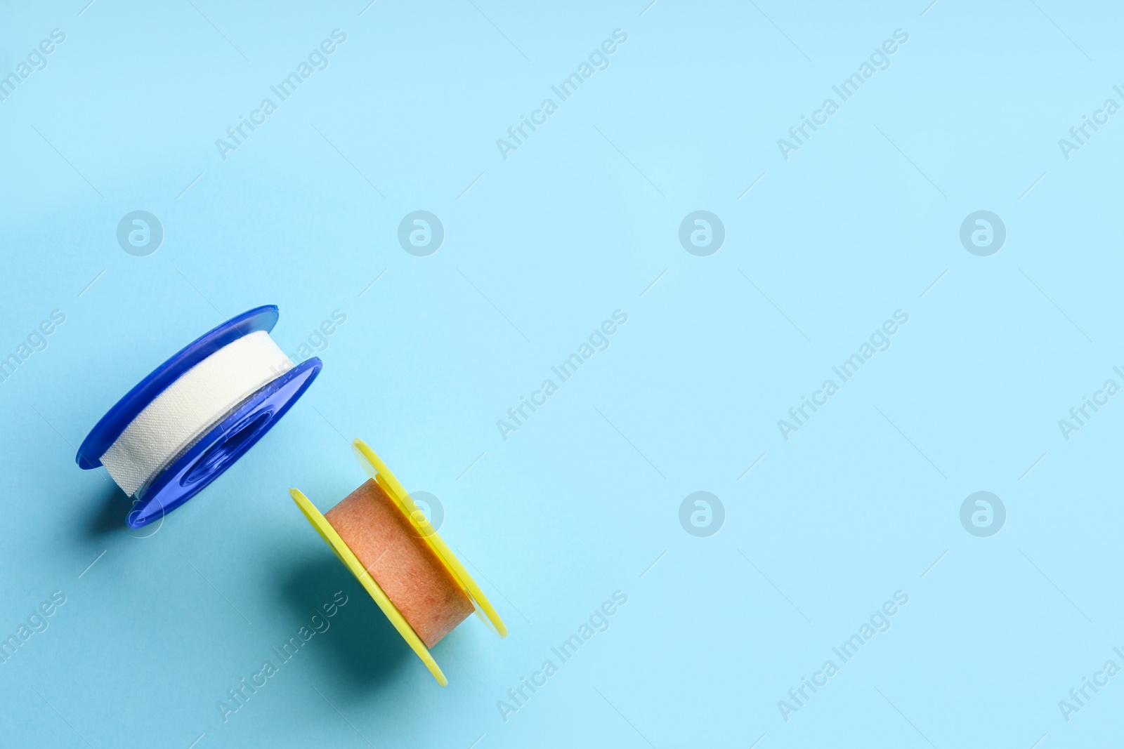 Photo of Sticking plaster rolls on light blue background, flat lay. Space for text