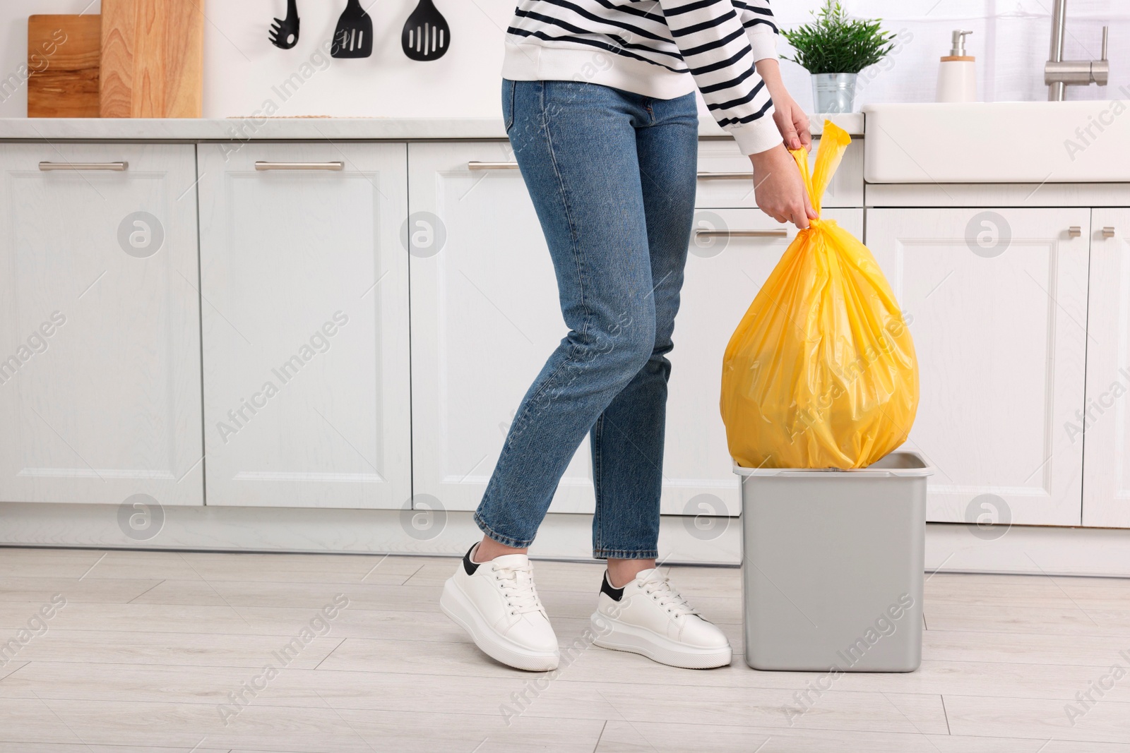 Photo of Woman taking garbage bag out of trash bin in kitchen, closeup. Space for text