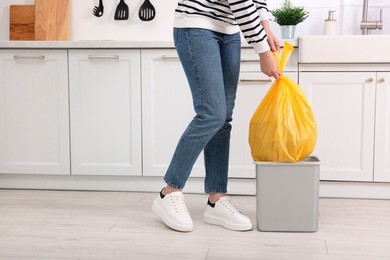 Photo of Woman taking garbage bag out of trash bin in kitchen, closeup. Space for text