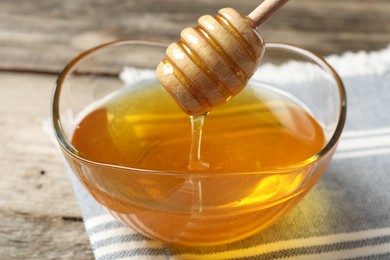 Photo of Delicious honey flowing down from dipper into bowl on wooden table, closeup