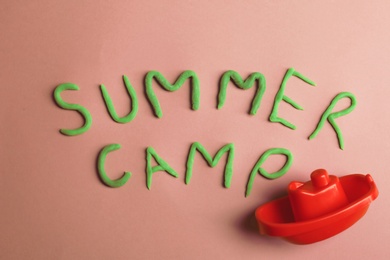 Photo of Words SUMMER CAMP made from modelling clay and plastic boat on color background, top view