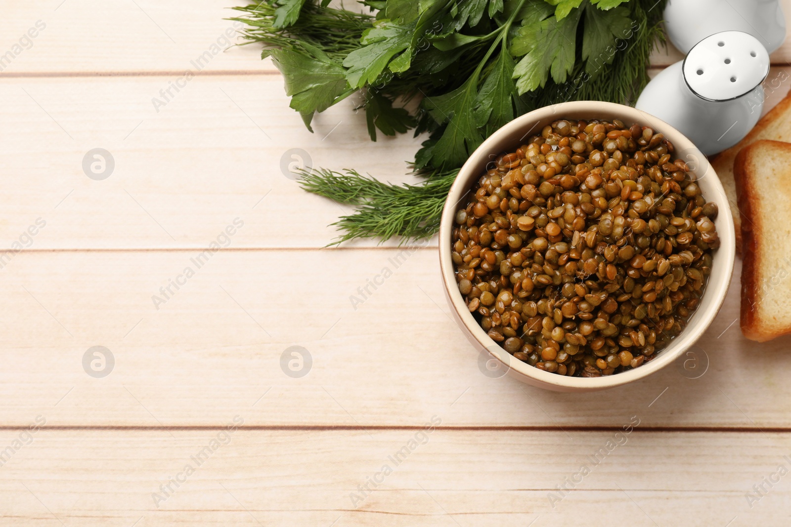Photo of Delicious lentils in bowl served with greens on wooden table, flat lay. Space for text