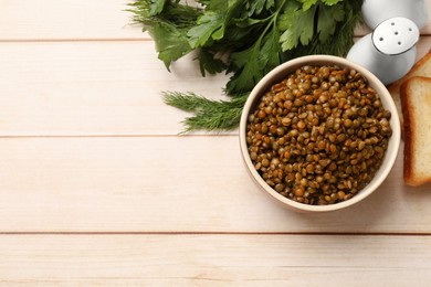 Delicious lentils in bowl served with greens on wooden table, flat lay. Space for text
