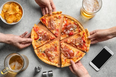 Photo of Young people taking slices of tasty pizza with meat at table, top view