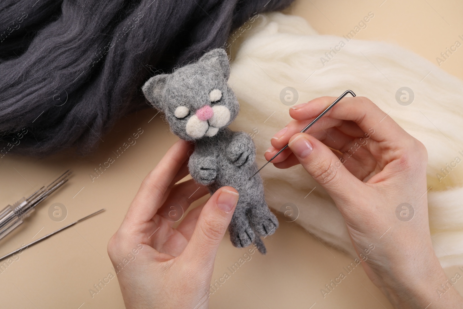 Photo of Woman felting cute toy cat from wool at beige table, closeup