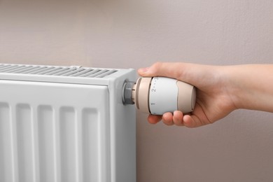 Photo of Girl adjusting heating radiator thermostat near white wall, closeup