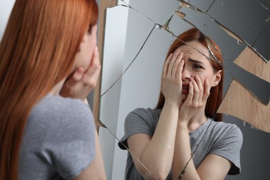 Photo of Emotional young woman suffering from mental problems near broken mirror