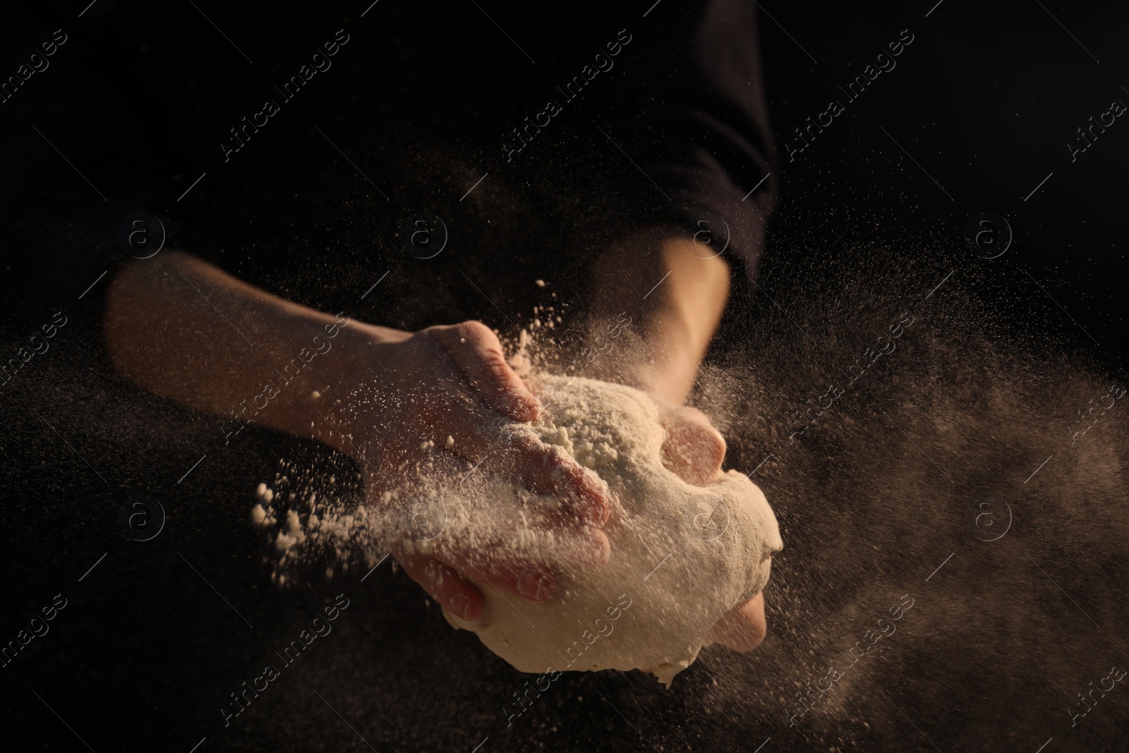 Photo of Making bread. Woman kneading dough on dark background, closeup