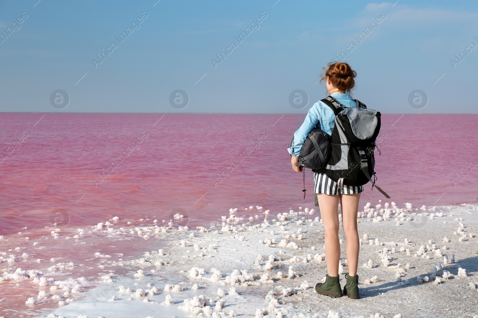 Photo of Woman with backpack and sleeping bag on coast of pink lake