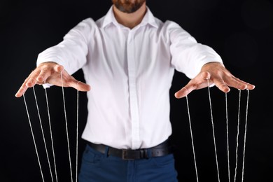 Photo of Man in formal outfit pulling strings of puppet on black background, closeup