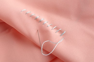 Photo of Sewing needle with thread and stitches on coral cloth, closeup