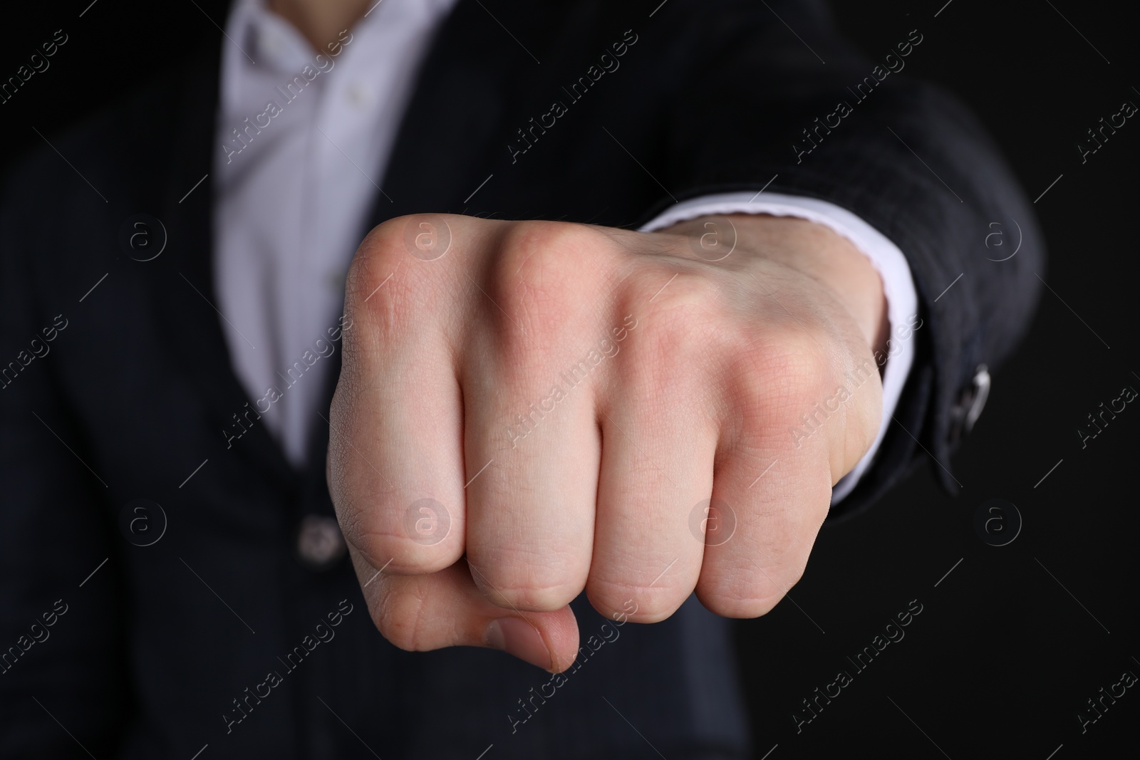 Photo of Businessman showing fist with space for tattoo on black background, closeup