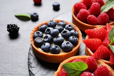 Tartlets with different fresh berries on black table, closeup. Delicious dessert