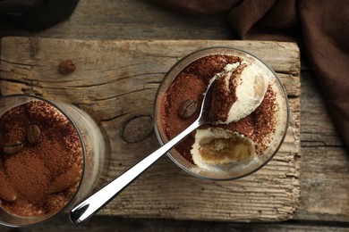 Delicious tiramisu in glasses, spoon and coffee beans on wooden table, top view