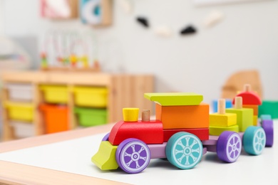 Photo of Colorful wooden toy locomotive on table in playroom, closeup. Space for text