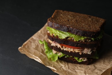 Photo of Delicious sandwich with tuna, tomatoes and lettuce on black table, space for text