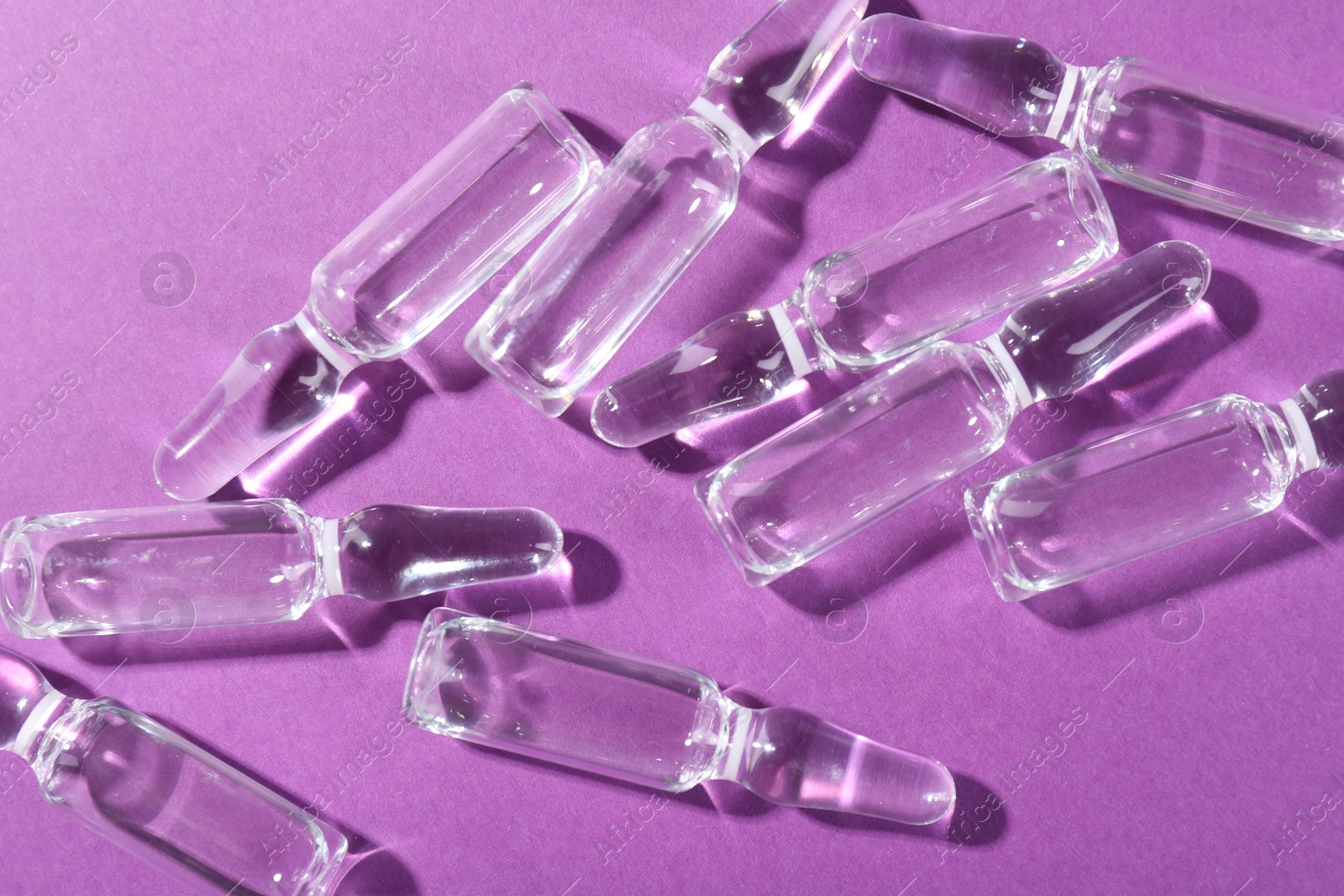 Photo of Glass ampoules with liquid on purple background, top view