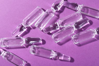 Photo of Glass ampoules with liquid on purple background, top view