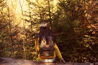 Woman with backpack sitting on log in autumn forest