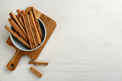 Photo of Aromatic cinnamon sticks on white wooden table, flat lay. Space for text